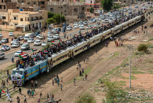 Photo of Sudanese revolutionaries on a train and traffic in the background.