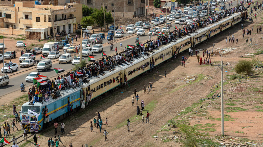 Photo of Sudanese revolutionaries on a train and traffic in the background.